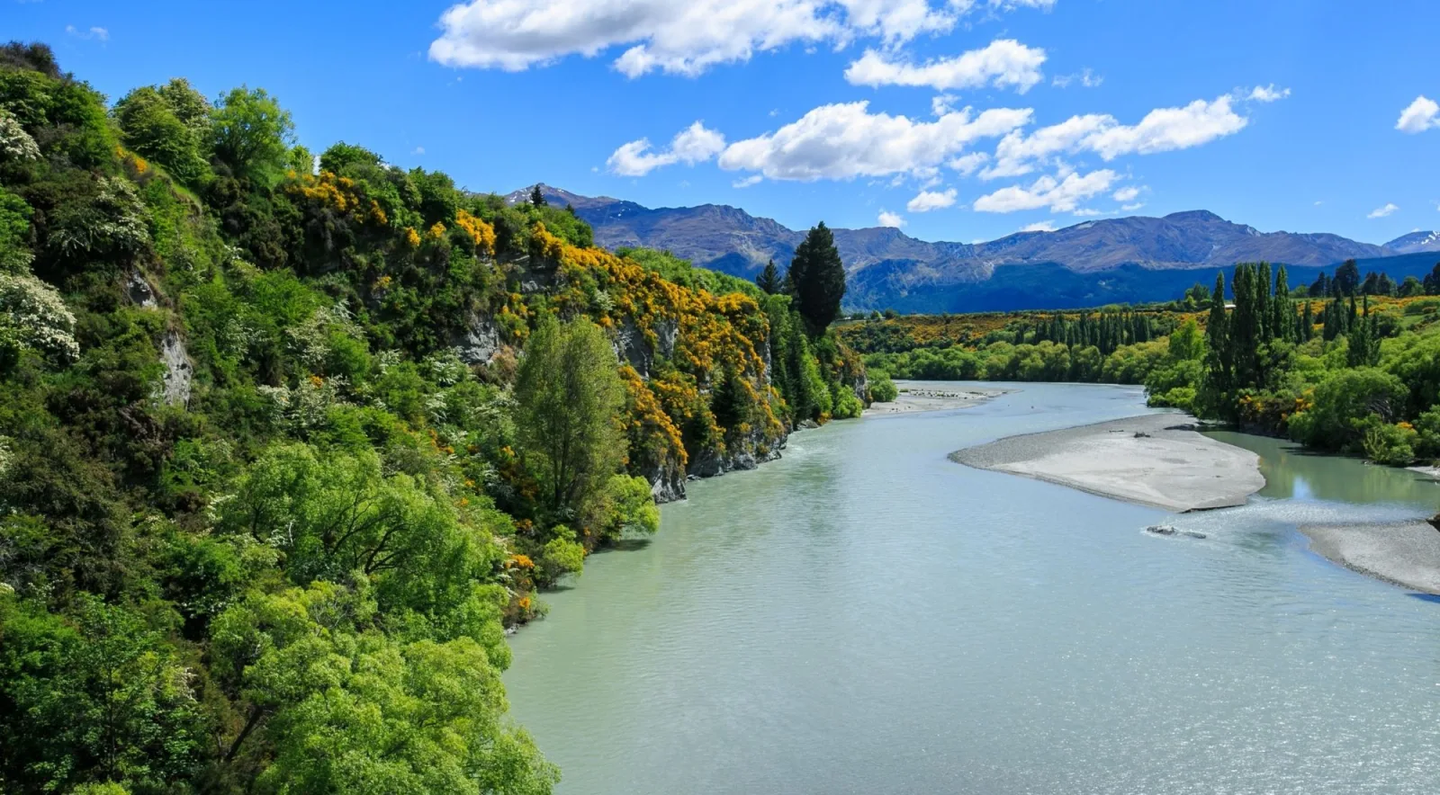 The Shotover River running pale green between wooded banks, with mountains behind