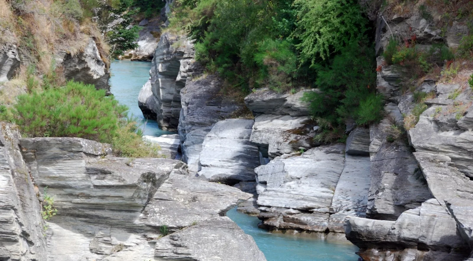 Layered grey schist walls squeezing a narrow channel of turquoise water