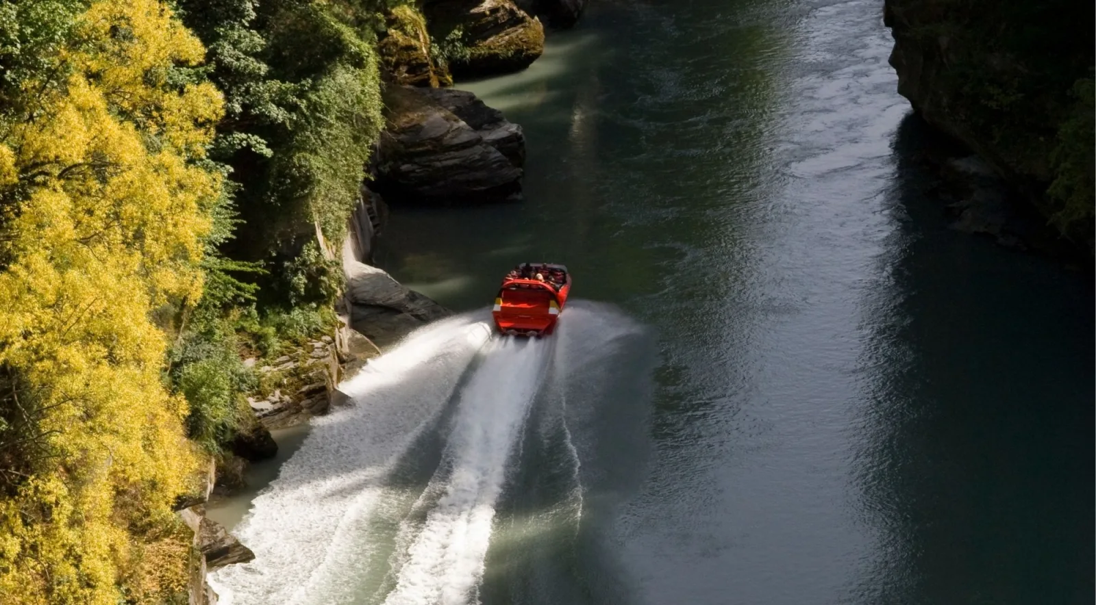 A red jet boat throwing a white wake as it runs a narrow canyon between rock walls