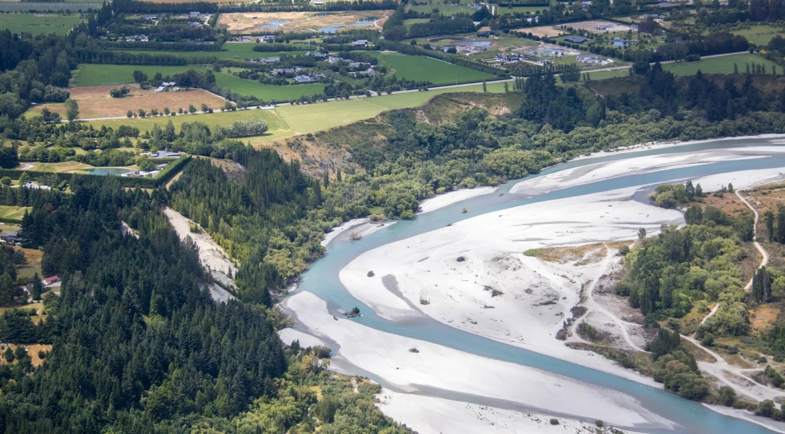 Aerial view of a braided river winding across a broad valley floor toward farmland