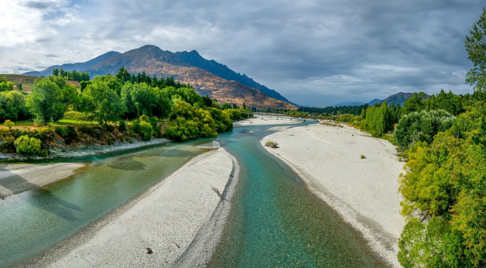A river curving around a long gravel spit under a heavy grey sky