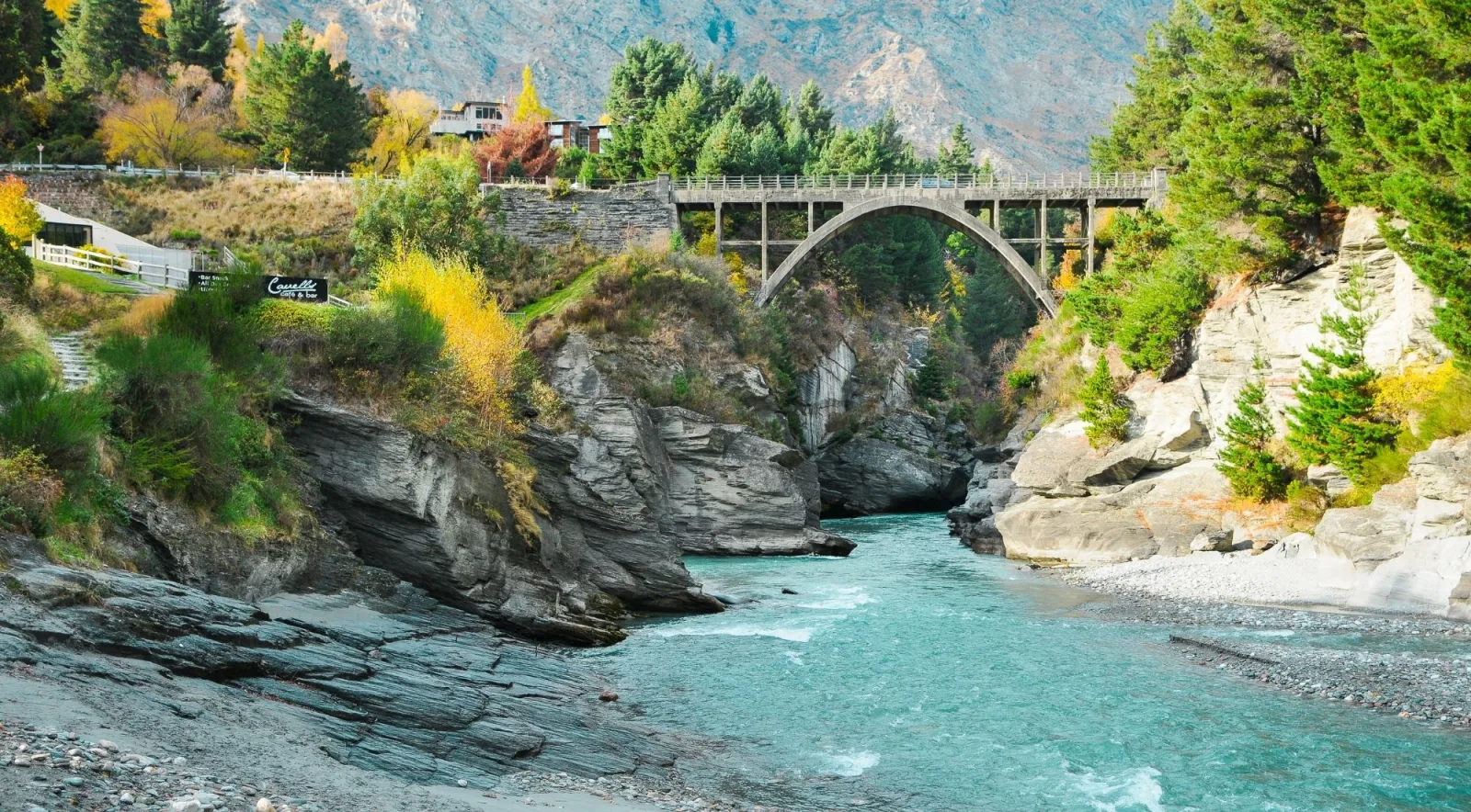 A stone arch bridge spanning a deep canyon above bright turquoise water