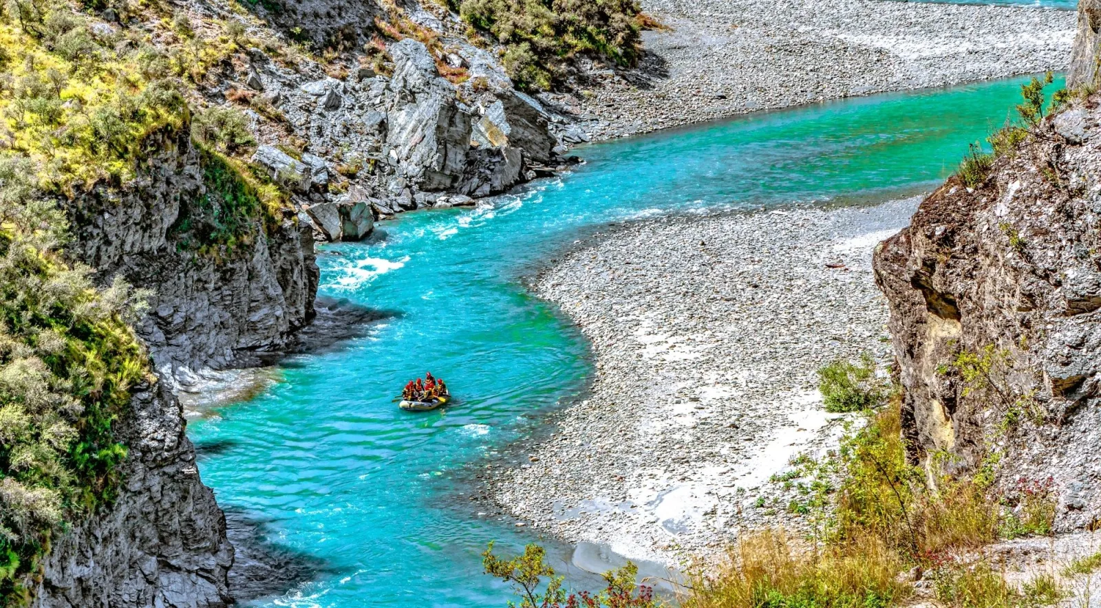 A raft on bright turquoise water in a rocky canyon with steep grey walls